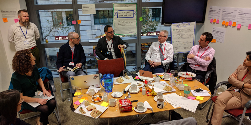 In a meeting room in MHCLG, 8 members of staff (including the 5 members of the expert panel) sit around a table discussing the shortlisted applications for the Local Digital Fund. 