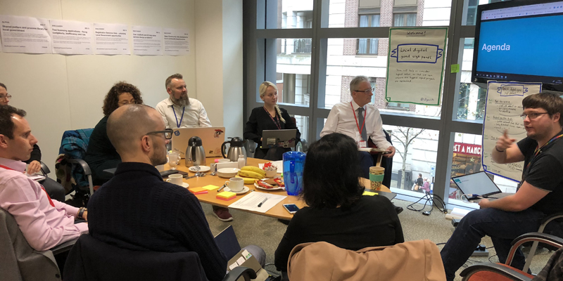 In a meeting room in MHCLG, 9 members of staff (including the 5 members of the expert panel) sit around a table discussing the shortlisted applications for the Local Digital Fund. 