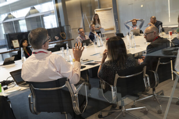 Tess O'Brien of Bloomberg Associates chairs a session during the workshop, standing at a flipchart and looking towards the discussion taking place around a table. Image courtesy of David Levenson.