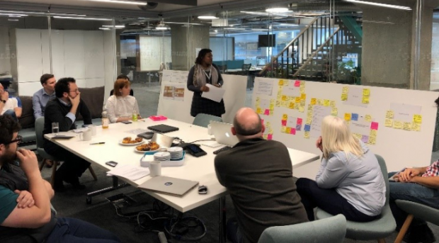 A photograph of a session from the 'Family Context in Children’s Services' project team, reviewing User Research with Social Workers around a whiteboard with post-it notes.