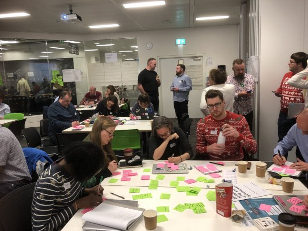 A photograph of people sat at tables writing on post-its notes at the Local Digital Fund kick-off workshop, hosted by MHCLG in December. Each of the 16 Local Digital Fund projects attended the workshop.