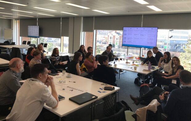 20 attendees in sat around tables in a group discussion, at the Local Digital collaboration roadshow in Coventry.