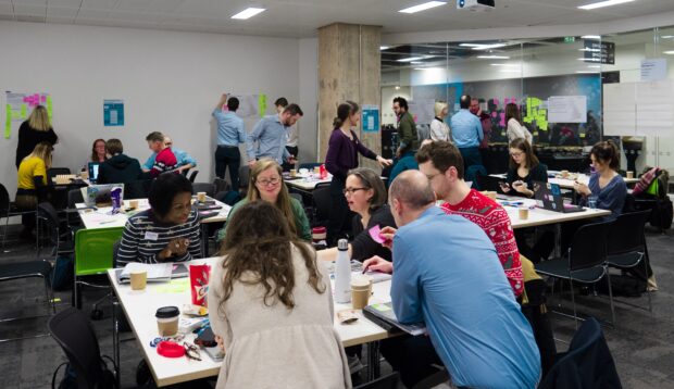 Members of the 16 collaborative Local Digital Fund project teams sit at tables in a large room, at the kick-off workshop in December.