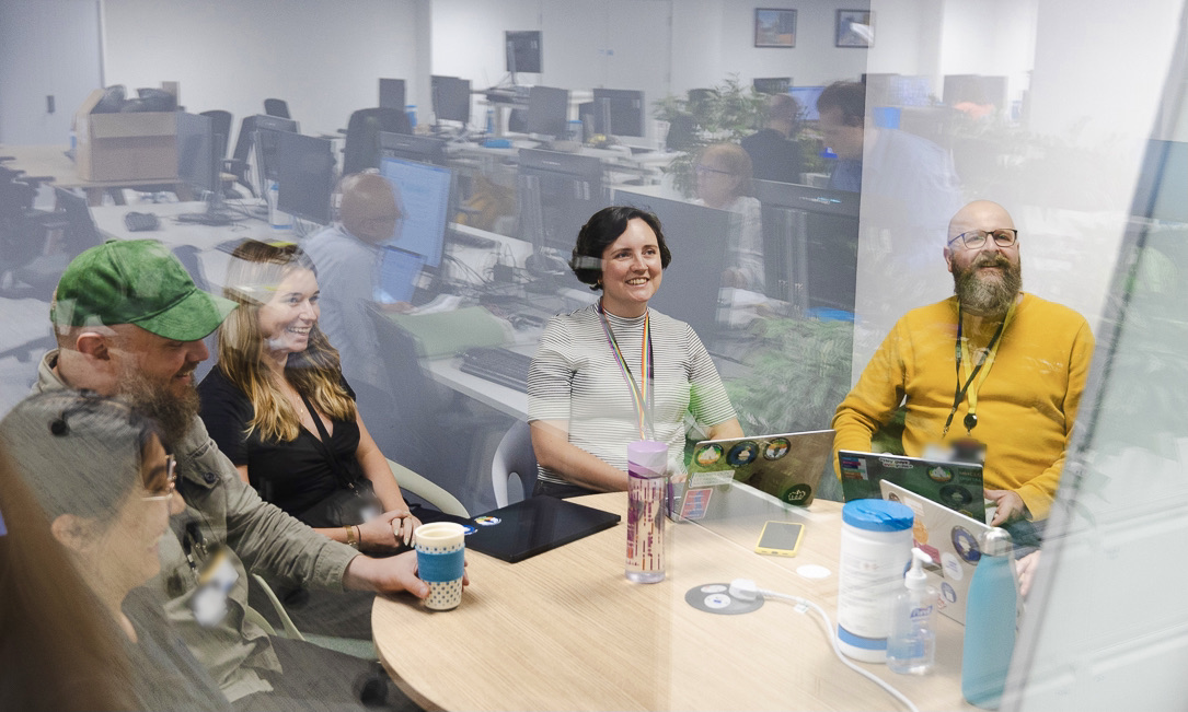 A digital team at DLUHC are sat around a table during a meeting