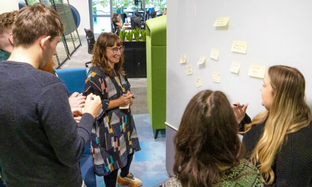 A group of colleagues standing together in front of a whiteboard and putting post-it notes on it and talking