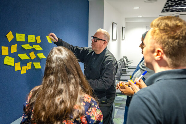 DLUHC Local Digital team brainstorming at their office in Birmingham - one person putting post-it notes on a wall and others looking