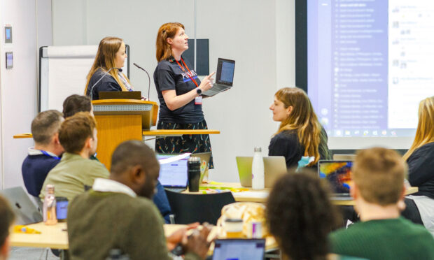 two people presenting in front of a screen, with others listening to their presentation 