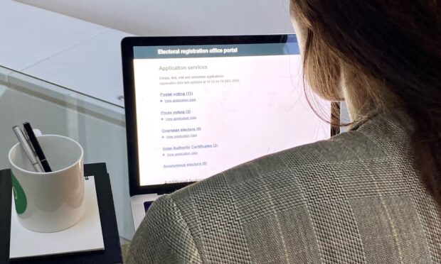 A person facing away from the camera sitting at a laptop with the screen showing the Electoral registration office portal website