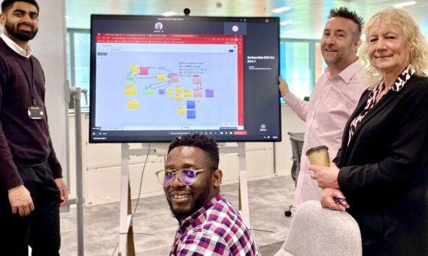 A group of people standing by a large screen showing a kanban board