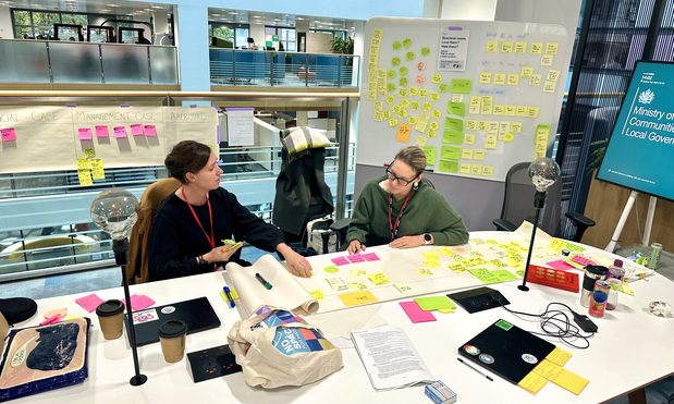 two colleagues, working at a desk together, looking at a mind map made of post it notes